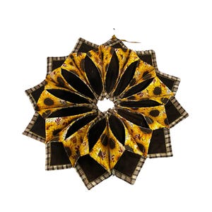 May include: A brown and yellow sunflower fabric wreath with a plaid trim. The wreath is made of fabric squares sewn together to form a circle.