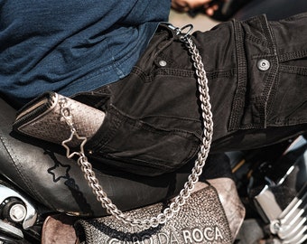 May include: A silver chain with a star charm attached to a wallet in a back pocket of black cargo pants.