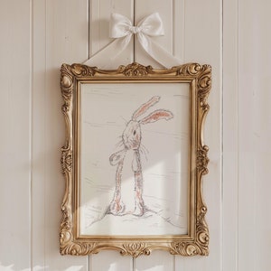 以下が含まれることがあります： 金色の額縁に白いリボンがかけられた絵。絵には白黒のウサギのイラストが描かれている。