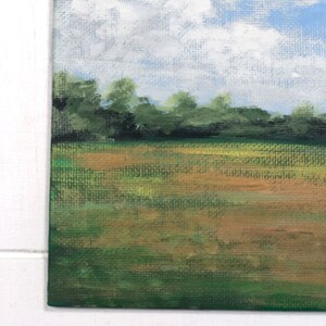 May include: A painting depicting a landscape with a field of green grass and a blue sky with white clouds. The trees in the background are a dark green.