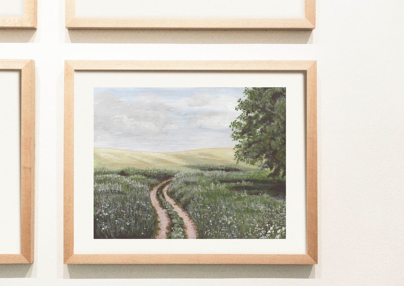 May include: A framed painting of a dirt road leading through a field of green grass and white flowers. A single tree stands on the right side of the road, with a blue sky and white clouds in the background.