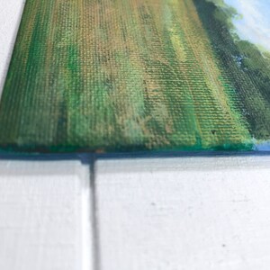 May include: Close-up of a green and brown canvas painting with a textured surface. The painting depicts a landscape with a field of grass and trees in the background.