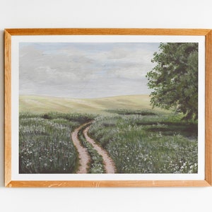 May include: A framed painting of a winding dirt road leading through a field of green grass and white wildflowers. The sky is a light blue with gray clouds. A large green tree stands on the right side of the road.