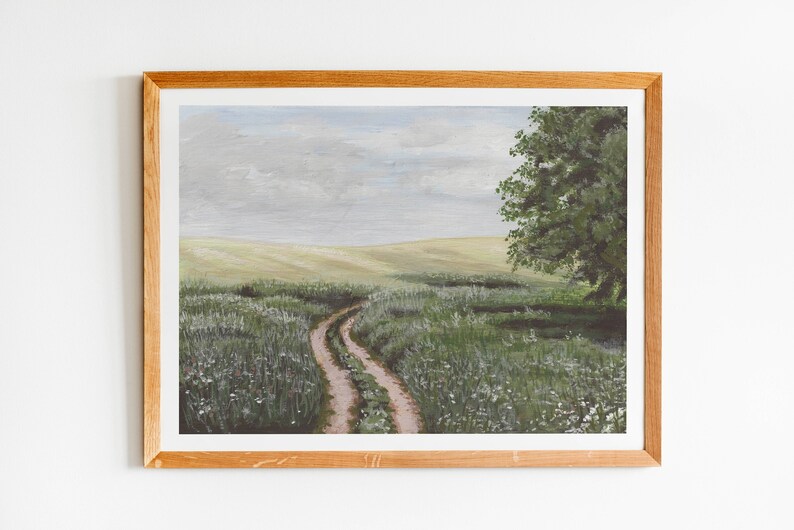 May include: A framed painting of a winding dirt road leading through a field of green grass and white wildflowers. The sky is a light blue with gray clouds. A large green tree stands on the right side of the road.