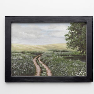 May include: A framed painting of a dirt road winding through a field of green grass and white wildflowers. The sky is cloudy and a single tree stands on the right side of the road.