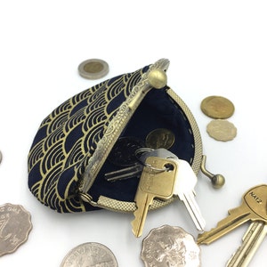 May include: A small, navy blue coin purse with a gold geometric pattern. The purse is open and has keys and coins inside. The purse has a brass clasp and a decorative metal rim.