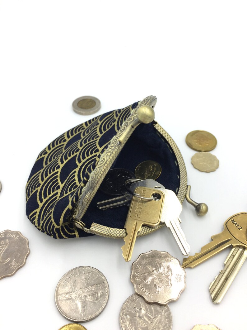 May include: A small, navy blue coin purse with a gold geometric pattern. The purse is open and has keys and coins inside. The purse has a brass clasp and a decorative metal rim.