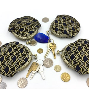 May include: Four round coin purses with a gold and black wave pattern. The purses have a brass clasp and are open. Keys and coins are scattered around the purses.