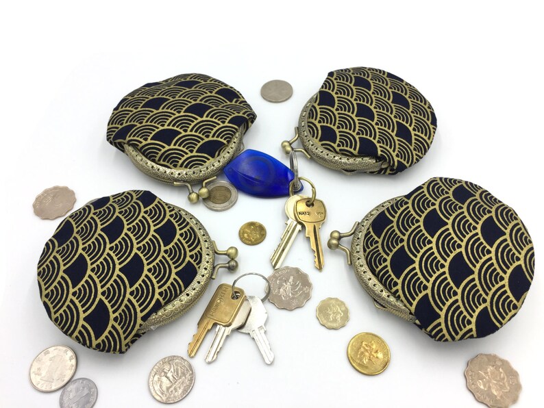 May include: Four round coin purses with a gold and black wave pattern. The purses have a brass clasp and are open. Keys and coins are scattered around the purses.