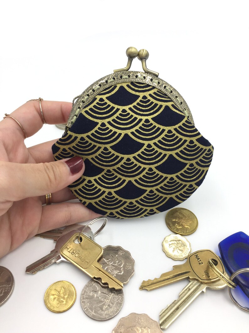 May include: A small, round coin purse with a gold and navy blue fabric exterior. The purse has a decorative metal clasp and a scalloped edge. The fabric features a repeating pattern of gold scales on a navy blue background.