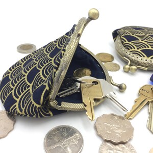 May include: A blue and gold coin purse with a wave pattern. The purse is open and has keys inside. There are also several coins scattered around the purse.