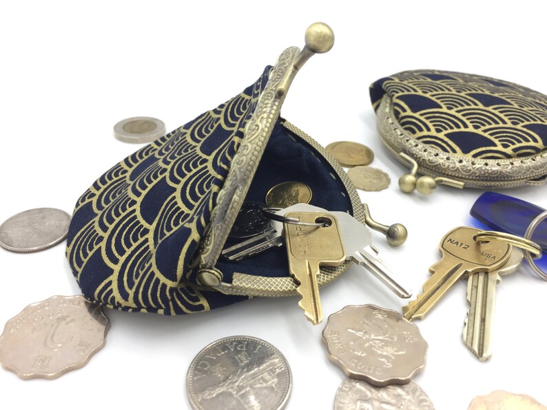 May include: A blue and gold coin purse with a wave pattern. The purse is open and has keys inside. There are also several coins scattered around the purse.