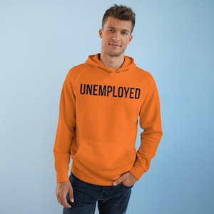 May include: Orange hoodie with the word "UNEMPLOYED" printed in black across the chest. The hoodie has a kangaroo pocket and a drawstring hood. The person is wearing dark blue jeans.