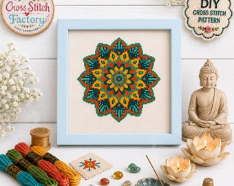 May include: A framed cross stitch pattern featuring a symmetrical mandala design in teal, orange, and yellow on cream fabric. The light blue frame surrounds the embroidery, accompanied by embroidery floss, a small needle, and a thimble.
