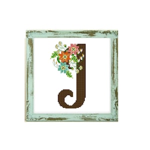 Puede incluir: Un patrón de punto de cruz con la letra J y un diseño floral. La letra es marrón y las flores son rosas, naranjas, azules y verdes.
