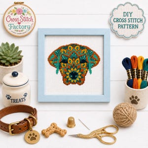 May include: A cross-stitch pattern of a dog head in a light blue frame, featuring geometric patterns in teal, orange, and yellow. Accessories include embroidery floss, a brown leather collar, a thimble, scissors, and a bone-shaped treat.