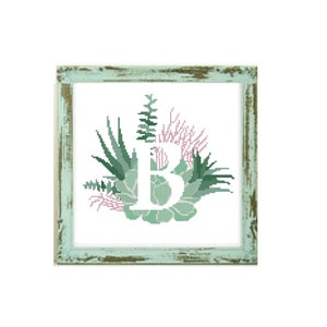 Könnte beinhalten: Kreuzstich-Kunstwerk mit dem Buchstaben "B", umgeben von grünen und rosa Sukkulenten. Das Design befindet sich vor einem weißen Hintergrund und ist in einem verwitterten, hellgrünen Holzrahmen gerahmt, was eine rustikale Ästhetik erzeugt.