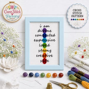 May include: A framed cross stitch pattern featuring a vertical stack of seven colored circles representing chakras, each paired with a word: divine, connected, expressive, loved, strong, creative, and safe, displayed in a light blue frame.