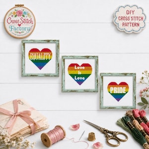 May include: Three square framed cross stitch pieces featuring rainbow-colored hearts with the words Equality, Love is Love, and Pride. Includes a round embroidery hoop with floral designs and the text Cross Stitch Factory, plus sewing supplies.