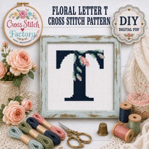 May include: A cross stitch pattern featuring a dark navy blue letter T decorated with pink and green floral motifs, displayed in a light blue distressed wooden frame. The design includes text reading Floral Letter T Cross Stitch Pattern.