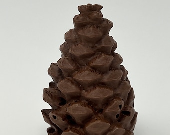 May include: A brown, 3D printed pine cone ornament. The ornament is detailed with a textured surface and has a small hole at the top for hanging.