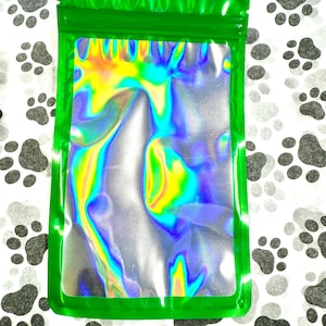 May include: A green resealable bag with a holographic iridescent interior. The bag is lying flat on a white surface with black paw prints.