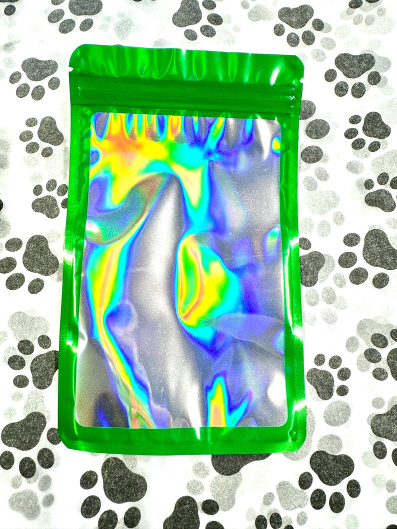 May include: A green resealable bag with a holographic iridescent interior. The bag is lying flat on a white surface with black paw prints.