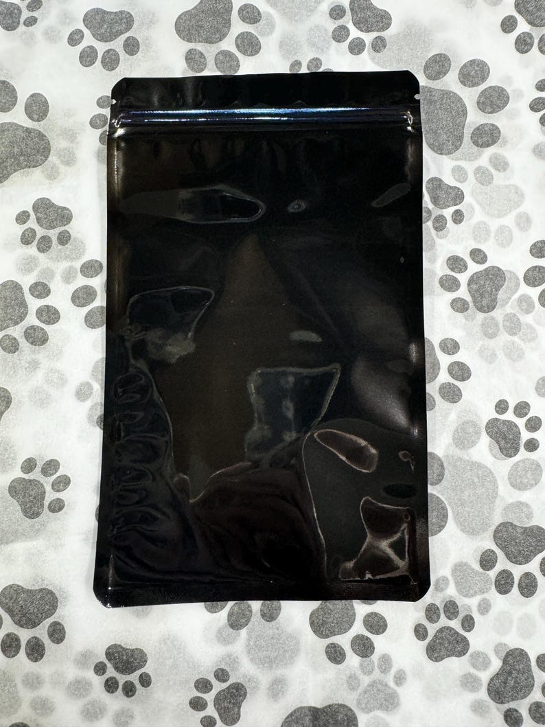 May include: A black, stand-up pouch with a zipper closure. The pouch is made of a shiny, metallic material.