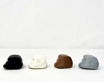 May include: Four small, rock-shaped salt and pepper shakers in black, white, brown, and grey.