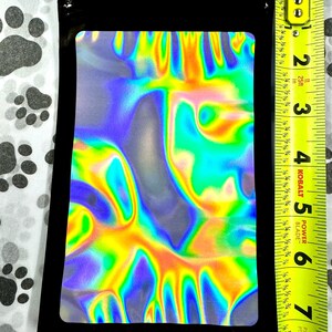 May include: A black zippered pouch with a holographic iridescent inner lining. The pouch is approximately 6 inches tall and 4 inches wide.