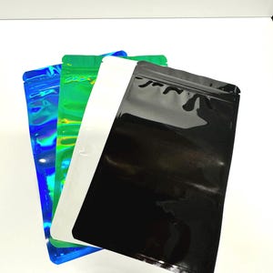May include: Three stand-up pouches, one iridescent blue, one green, and one black. The pouches are made of a shiny, plastic-like material and have a zipper closure.