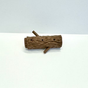 May include: A brown wooden log with three holes drilled into it. The log has two small branches extending out from the sides.