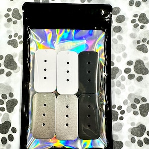 May include: A package of six blank metal dog tags in three different colors: white, silver, and black. The tags are rectangular with rounded corners and have four holes for attaching a chain or other hardware.