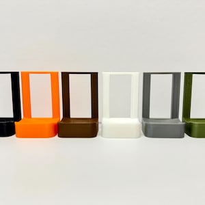 May include: Six different colored plastic stands, each with a rectangular opening. The stands are black, orange, brown, white, gray, and green.