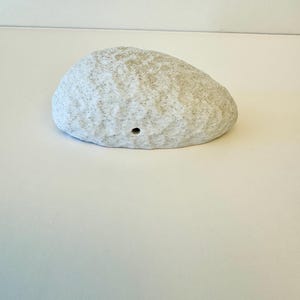 May include: A white ceramic rock with a rough texture and a small hole in the center.