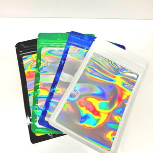 May include: Four iridescent holographic mylar bags with zipper closures. The bags are stacked on top of each other, with the white bag on top, followed by a blue bag, a green bag, and a black bag.