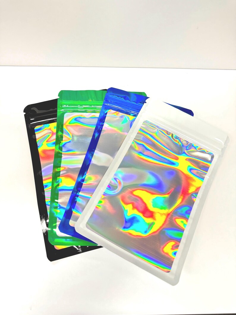 May include: Four iridescent holographic mylar bags with zipper closures. The bags are stacked on top of each other, with the white bag on top, followed by a blue bag, a green bag, and a black bag.