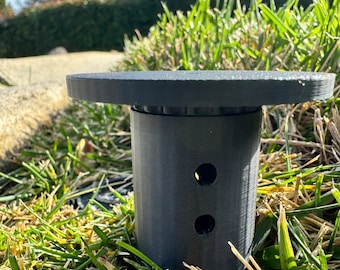 May include: A black plastic sprinkler head with two holes for water dispersal, sitting on a bed of green grass.