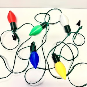 May include: A string of five miniature Christmas lights with a green cord. The lights are red, green, white, blue, and yellow.