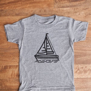 May include: A gray t-shirt with a black sailboat graphic.