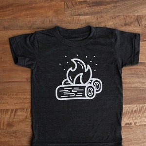 May include: A dark gray t-shirt with a white graphic of a campfire with flames and logs.