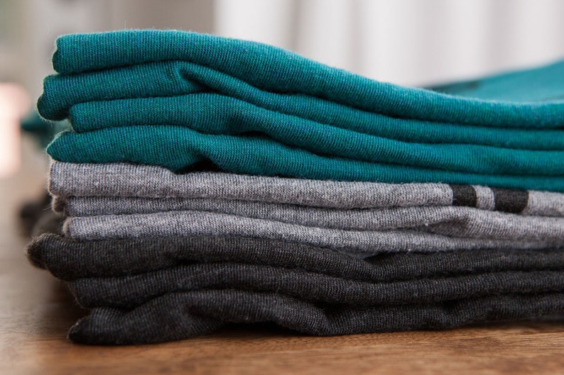 May include: A stack of folded t-shirts in teal, gray, and black.