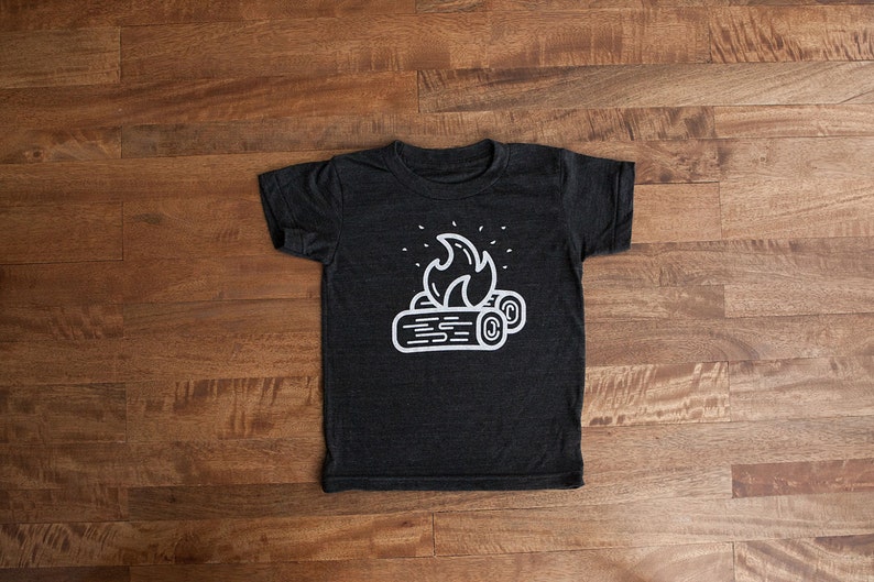 May include: A dark gray t-shirt with a white graphic of a campfire with flames and logs.