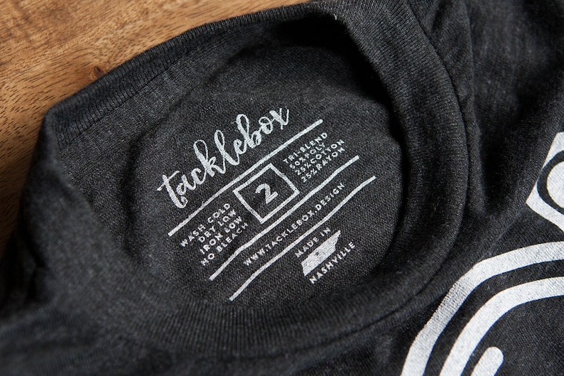May include: A black t-shirt with a white tag that says "tacklebox" and includes care instructions, size 2, website address, and "Made in Nashville".