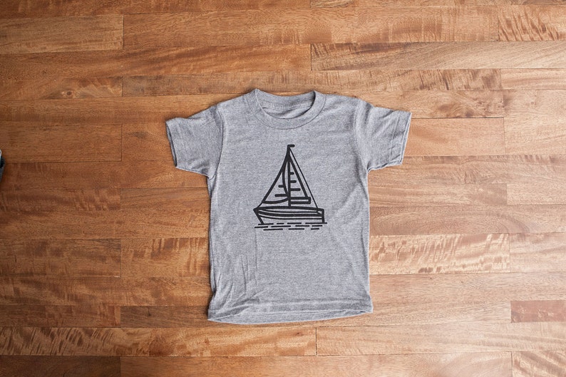 May include: A gray t-shirt with a black sailboat graphic.