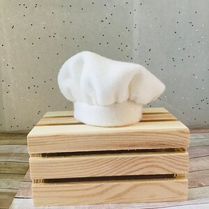 Pu&ograve; includere: Un cappello da chef bianco in feltro su una cassa di legno.