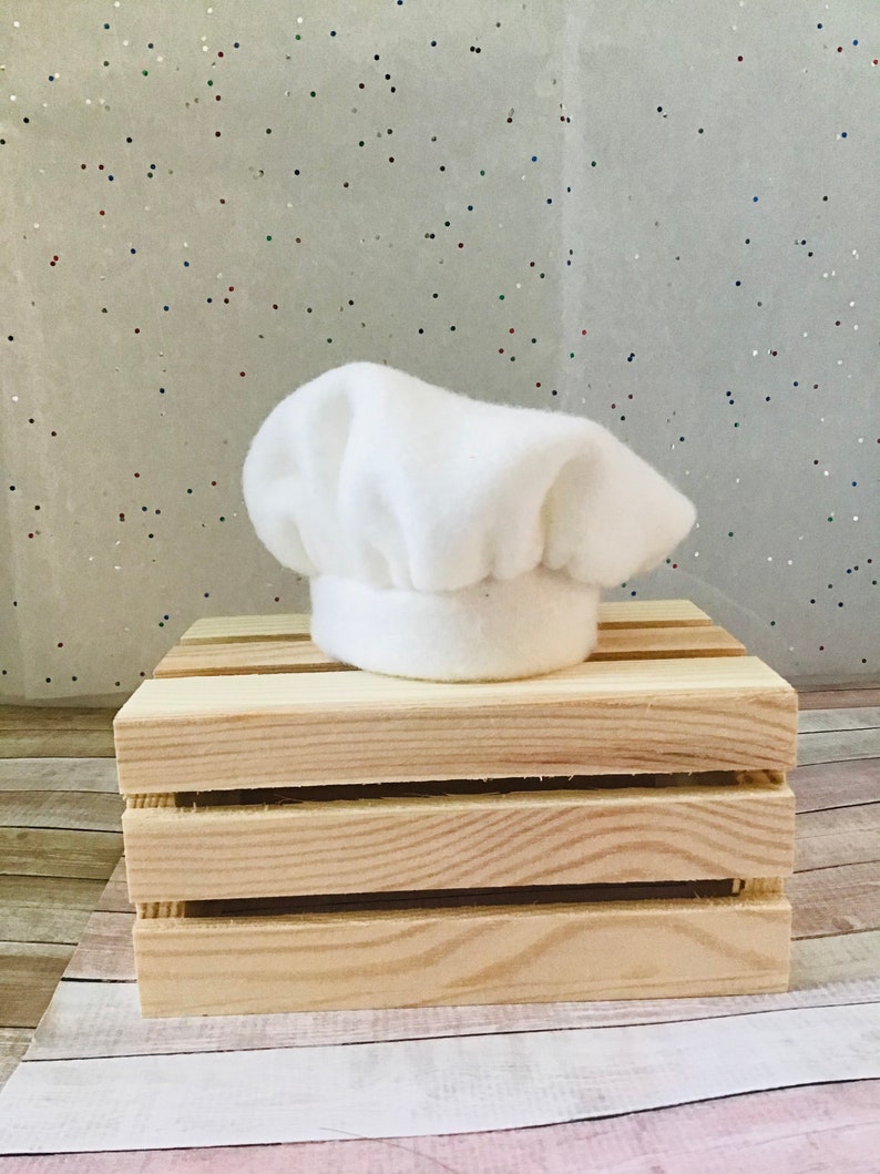 Pu&ograve; includere: Un cappello da chef bianco in feltro su una cassa di legno.