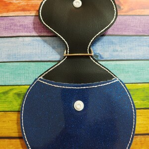 Może przedstawiać: Niebieska błyszcząca portmonetka na monety z czarną g&oacute;rą z imitacji sk&oacute;ry i białym zatrzaskiem. Portmonetka ma biały obszyty brzeg.