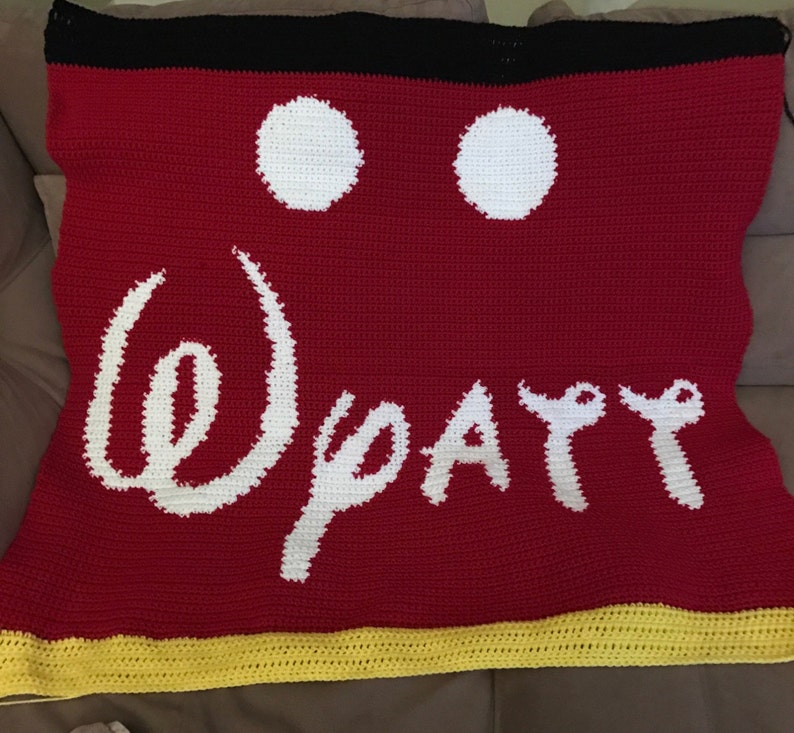May include: Red crocheted blanket with a white Mickey Mouse head design and the words "Disney" in white. The blanket has a yellow border.