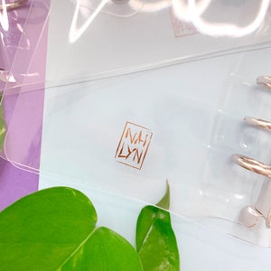 May include: A clear plastic binder with a gold foil logo that says "NAH LYN" on the front.